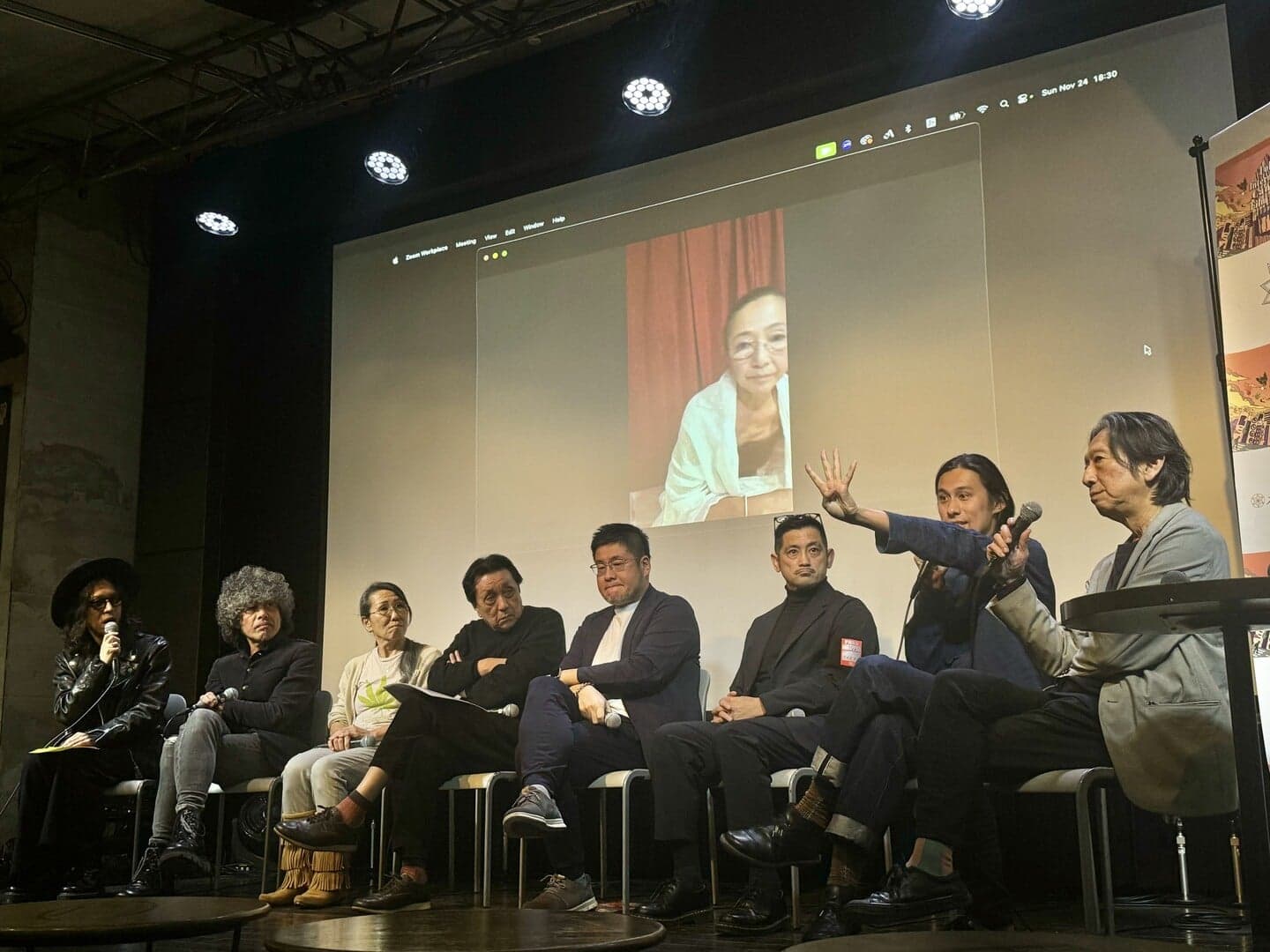 Panellists seated on stage alongside a guest joining by video link on the screen behind them